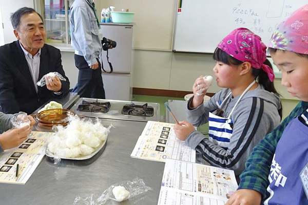 炊飯実習で作ったおにぎりを農家さんと一緒に味わう子供たちの画像